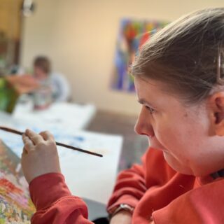 Amy Fenton in the gallery focused on a canvas in front of her.