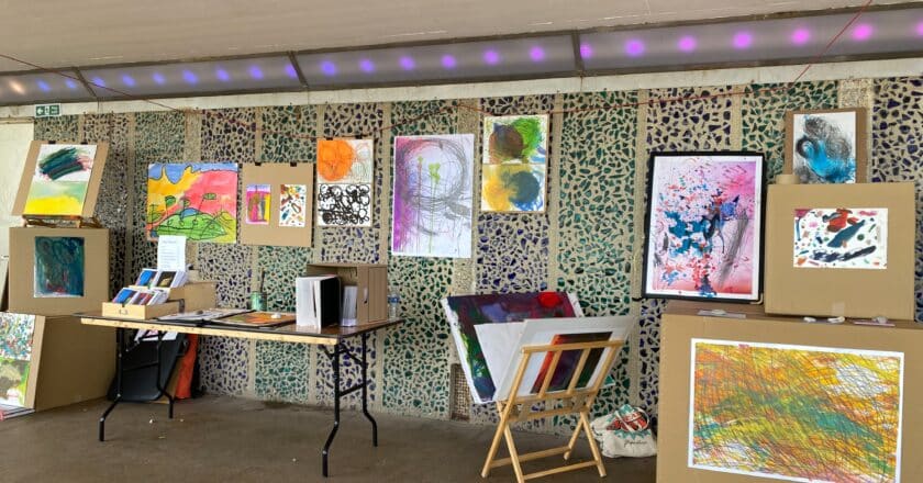 A stall of art works is set up on a table, easels and pinned to cardboard boxes.