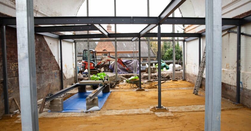 The photo shows the internal view of the arch 3 development at Project Art Works. Large grids are in place that will support floors and walls in the build. The floor is made of sand waiting the floor to be built in. Construction tools lay about the site.