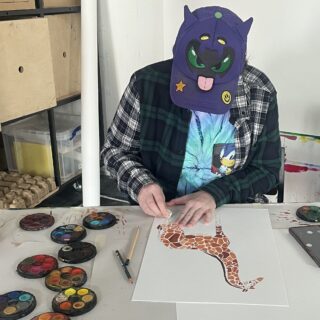 Bear sits at a desk working on a drawing of a giraffe.