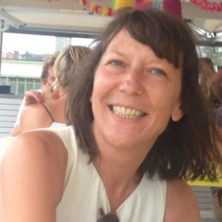 Gaby has short bobbed brown hair and is wearing a whit top. Gaby is smiling at the camera.