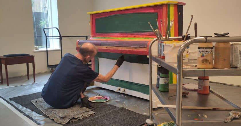 Mark decorates a piano in the studio. He is painting the piano in bright bold colours.